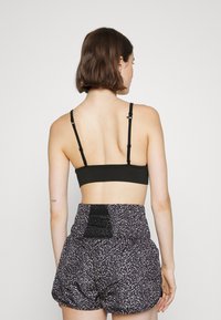 Bralette preta canelada com alças ajustáveis, combinada com calções de cintura alta estampados em tons escuros, apresentando uma cintura texturizada.