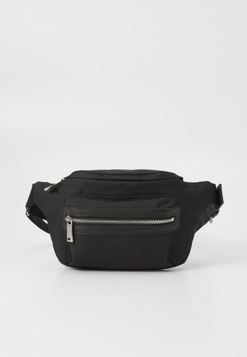 Juodas audinys fanny pack'as su užtraukiamu priekiu, reguliuojama juosta ir minimalistiniu dizainu. Yra tvirtas medžiaga ir elegantiška tekstūra.