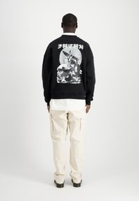 Felpa nera con grafica bianca sul retro, che presenta un personaggio e onde. Abbinata a pantaloni cargo beige chiaro e una camicia bianca.