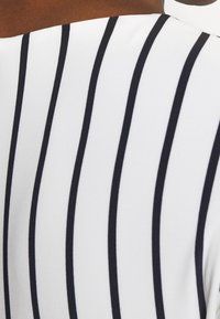 Vitt tyg med svarta vertikala ränder, med en slät textur. Designen är enkel och visar en modern och ren estetik.