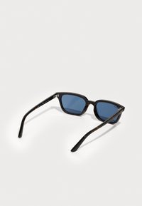 Lunettes de soleil en écaille noire avec monture rectangulaire, verres bleus et branches fines ornées d'accents métalliques.