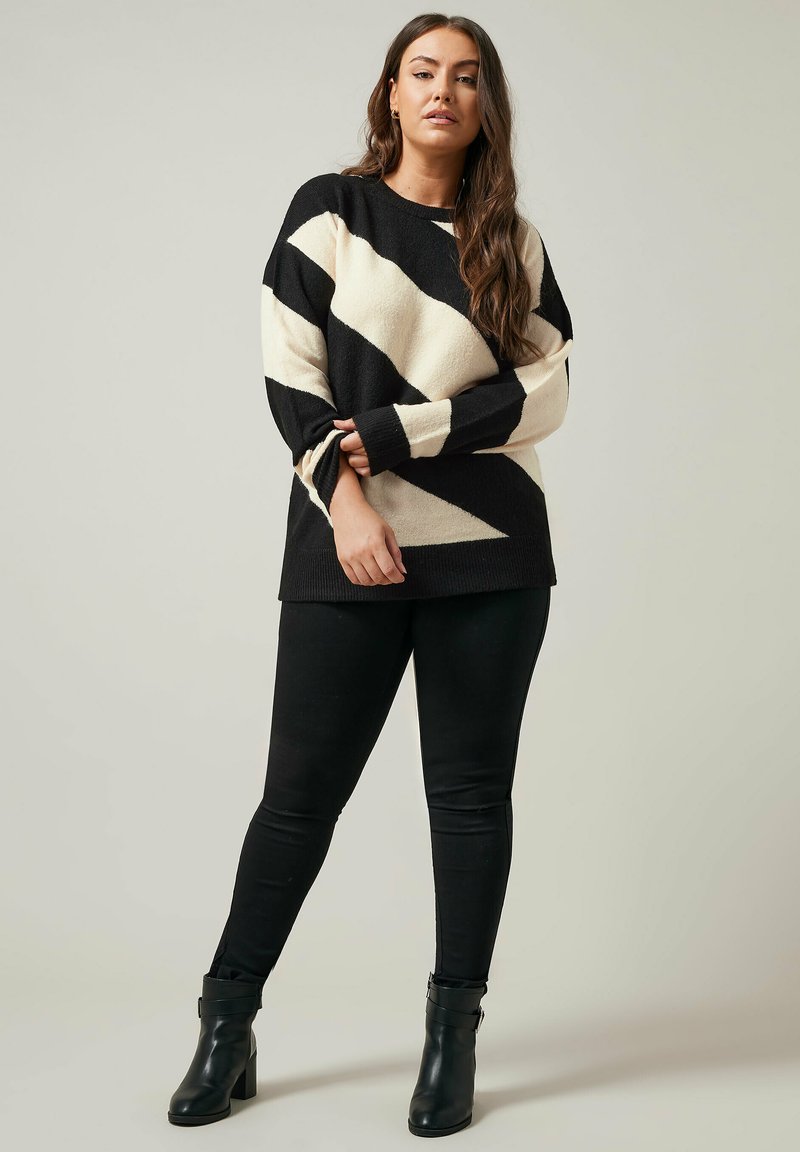 Pull noir et crème à motifs avec des rayures diagonales, à manches longues et à coupe décontractée. Porté avec un jean skinny noir et des bottes à talons.