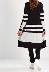 Lange, gestreepte tuniek in zwart en grijs, met horizontale strepen en een relaxed fit, gecombineerd met zwarte broeken en witte sneakers.