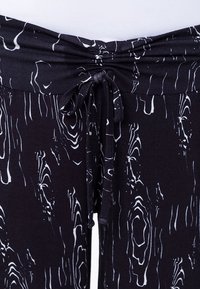 Svarta byxor med vitt vågigt mönster, utrustade med en sammanknuten midja och justerbar dragsko för en säker passform. Slät, elastisk tyg.