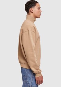 Felpa beige a maniche lunghe con colletto alto a costine. Presenta una vestibilità rilassata, una texture morbida e cuciture minime per un aspetto pulito.