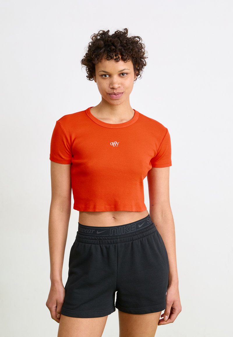 Kuttet oransje ribbet t-skjorte med korte ermer og frontlogo, sammen med svarte sweatshorts med elastisk midje og logo.