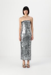 Sudraba strapless kleita ar čūskādīm rakstu. Gluda, spīdīga tekstūra, līdz ceļgaliem. Saskaņota ar melnām sandālēm ar siksniņām.