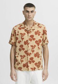 Camisa de botones de manga corta en beige con grandes patrones florales rojos. Presenta un cuello y un corte relajado, adecuada para el uso diario.