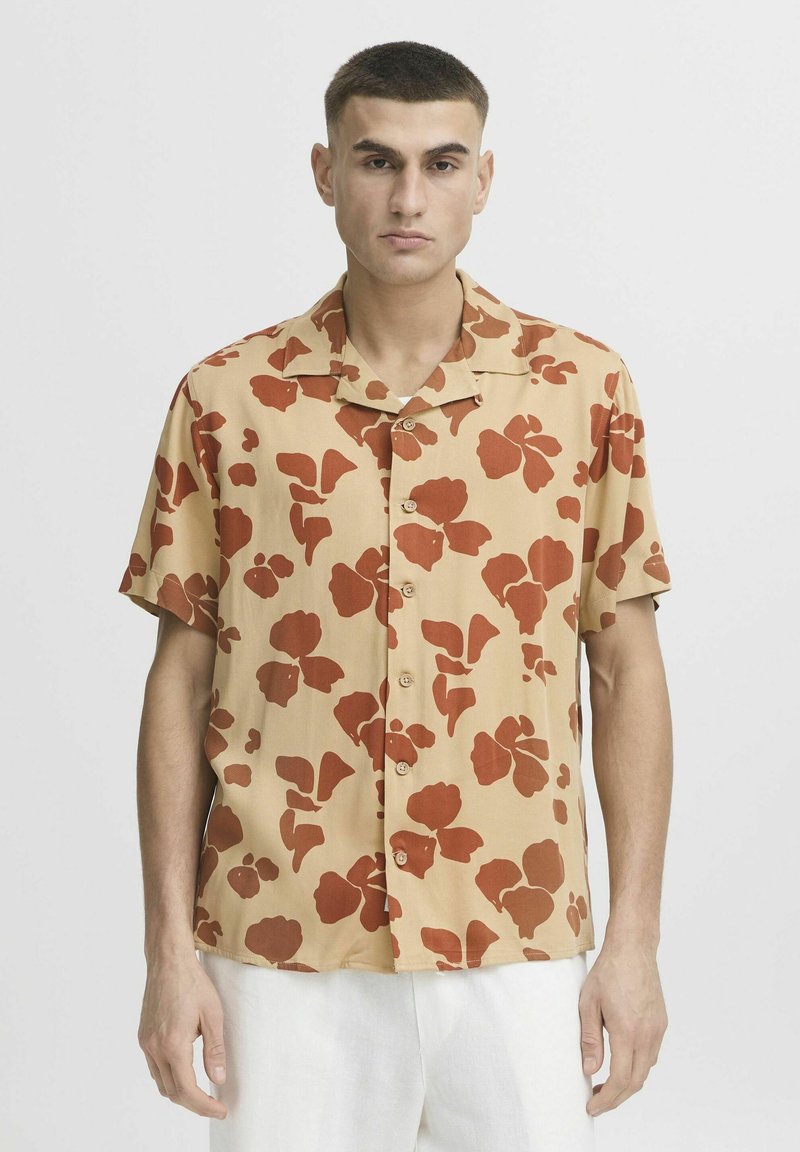Camisa de botones de manga corta en beige con grandes patrones florales rojos. Presenta un cuello y un corte relajado, adecuada para el uso diario.