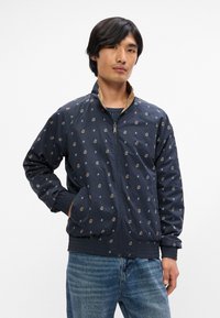 Ναυτική μπόμπερ τζάκετ με floral σχέδιο, κλείσιμο με φερμουάρ, ριμπ μανσέτες και καφέ γιακά. Απαλή υφή με ελαφρύ αίσθημα.