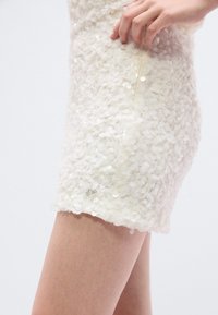 Λευκό φόρεμα με υφή επιφάνειας από μικρές, επικαλυπτόμενες παγιέτες. Διαθέτει πλαϊνή τσέπη και μικρό ασημένιο λογότυπο στο τελείωμα.