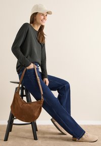 Ciemnoszara koszula z długim rękawem, niebieskie dżinsy, beżowa czapka, brązowa zamszowa torebka oraz jasnobeżowe buty wsuwane na czarnym stołku. Neutralne tło.