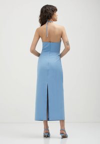 Ein blauer Halterhalsdress mit einem taillierten Oberteil, Reißverschluss auf der Rückseite und einem Schlitz hinten. Der Stoff wirkt glatt und strukturiert, mit einer langen Länge.