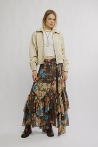Bež bomber jakna preko bijele majice, uparen s lepršavom, slojevitom smeđom suknjom s cvjetnim uzorkom u plavim i ružičastim nijansama te smeđim gležnjačama.