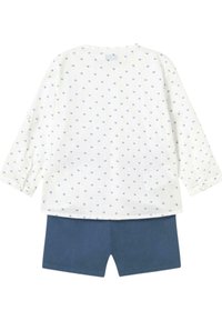 Camisa blanca de manga larga con lunares azules, combinada con pantalones cortos azul oscuro. La camisa tiene detalles de botones en las mangas. Tejido de algodón.