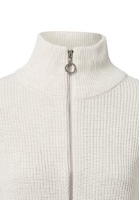 Maglione bianco a coste con colletto alto e una zip intera con un tirante circolare. Il tessuto ha un aspetto morbido e strutturato.