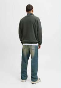 Dark green fleece jacket with a high collar, paired with loose, faded blue jeans and light-colored sneakers. The fabric appears soft.