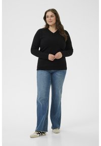 Pulover negru cu decolteu în V, dintr-un material moale, asortat cu blugi deschiși la culoare, evazați, având o croială lejeră, completat cu adidași bej.