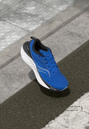 Chaussure de course bleue avec un dessus en maille texturée, semelle intermédiaire blanche arrondie et accents noirs. Comprend des lacets et un logo sur le côté.