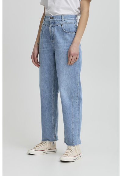 Jeans de tiro alto en azul claro con un diseño de pierna recta y acabados sin dobladillo, combinados con zapatillas beige. Fabricados en tela de denim sin patrones visibles.