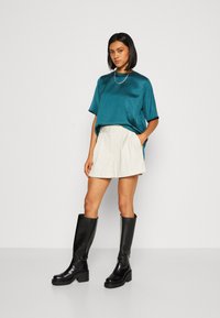 Teal satin top med korte ærmer, parret med en cremefarvet plisseret mini-nederdel og knæhøje sorte læder platform støvler. Sølv kædedesign inkluderet.