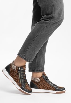 Person trägt mittelhohe Sneakers mit Leopardenmuster und schwarzer Einfassung, kombiniert mit dunkelgrauen Jeans vor weißem Hintergrund.