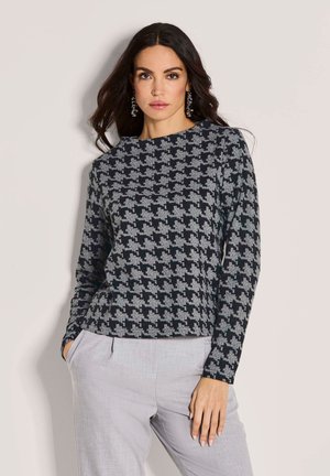 Schwarzer und grauer Hahnentritt-Muster-Strickpullover mit langen Ärmeln, rundem Ausschnitt und geradem Schnitt, kombiniert mit hellgrauen Hosen.