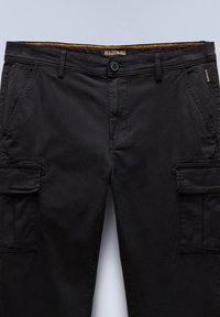 Czarne spodnie typu cargo wykonane z bawełny, z wieloma bocznymi kieszeniami, zamkiem błyskawicznym oraz kontrastującym żółtym wewnętrznym paskiem w talii.