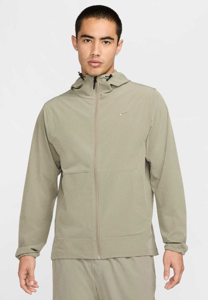 Veste à capuche zippée gris clair avec des poignets élastiques, des poches latérales et un logo discret sur la poitrine. Tissu lisse avec une finition mate.