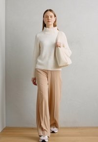 Pull à côtes blanc, pantalon large beige et sac à épaule beige clair. Le mannequin porte des baskets avec un mélange d'accents blancs et foncés.