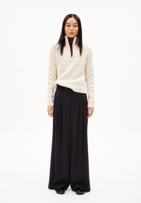 Pullover a maglia color beige chiaro con colletto a mezza zip abbinato a pantaloni larghi a righe blu navy, caratterizzati da una finitura testurizzata e una vestibilità rilassata.