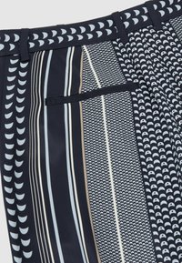 Tumesinised püksid valgete poolringi- ja vertikaalsete triipude mustriga, millel on vööaugud ja üks horisontaalne lõhke tasku.