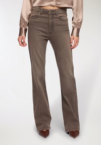 Brązowe dżinsy flare z wysokim stanem. Tkanina ma lekki po�łysk i subtelną fakturę, z klasycznymi kieszeniami i szlufkami na pasek.