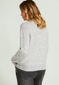 Jasnoszary sweter o luźnym kroju, z dzianą fakturą i prążkowanym dołem. Tył ozdobiony jest ażurowym wzorem w okolicach ramion.