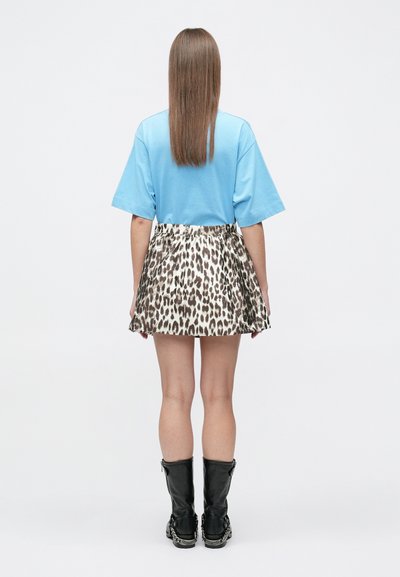 Une personne aux longs cheveux bruns se tient de dos, portant une chemise à manches courtes bleu clair, une jupe à imprimé léopard et des bottes noires montant jusqu'au milieu du mollet.