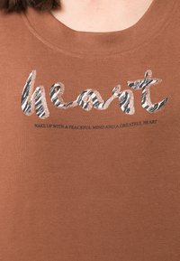 Brun bomulds t-shirt med et glitrende zebrastribet "hjerte" design og trykt tekst: "VÅGN OP MED ET FREDYGTIGT SINNED OG ET TAKNEMLIG HJERTE."