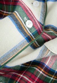 Bordo, žalia, raudona ir mėlyna plaid flanelinė marškinė cream spalvos su baltais mygtukais; turi minkštą tekstūrą ir kontrastingą žalią apdailą aplink apykaklę.