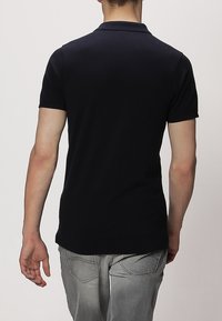 Czarna koszulka polo z krótkimi rękawami i kołnierzykiem, wykonana z gładkiego bawełnianego materiału, dopasowany fason, prezentowana od tyłu.
