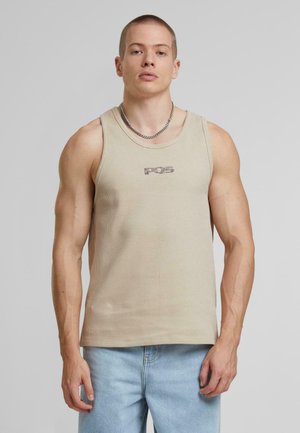 Débardeur à rayures beige avec un col rond, portant un petit logo sur la poitrine. Associé à un jean en denim bleu clair.