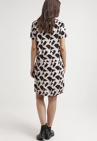 Korta ärmar klänning gjord av lättviktsmaterial med ett geometriskt svart och beige mönster. Den har en avslappnad passform och rund halsringning.