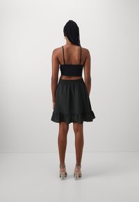Černý zkrácený top na tenké ramínka v kombinaci s černou sukní s volány. Oblečení má texturovanou látku a přiléhající pas.