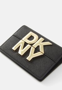 Čierna textúrovaná peňaženka so skladaným dizajnom, na prednej strane s výrazným zlatým písmom "DKNY". Hladký povrch, kompaktné rozmery.