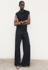 Black, short-sleeve top and long, wide-leg trousers made from a smooth fabric. Accessories include multi-colored bangles. Minimalist design.