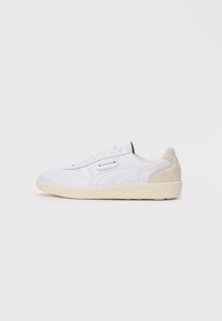 Hvite lavtopp sneakers med beige semsket hæl, snøring og teksturert beige såle på hvit bakgrunn.