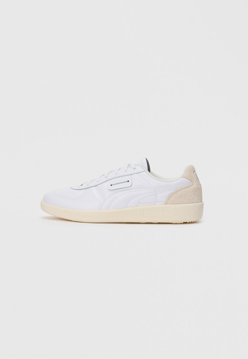 Hvite lavtopp sneakers med beige semsket hæl, snøring og teksturert beige såle på hvit bakgrunn.