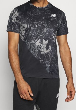 Mężczyzna w czarnej koszulce New Balance z abstrakcyjnymi szaro-czarnymi wzorami oraz dopasowanych czarnych szortach z białym logo New Balance.