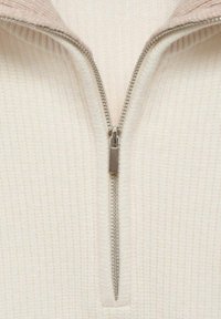 Svetr na zip v jemné krémové látce s texturovaným žebrovaným vzorem. Má kontrastní světle růžový límec a stříbrné zipové kování.