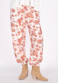 Bloemdruk broek in het wit met rood-oranje bloemen, gathered cuffs en een lichtgewicht, getextureerde stof. Gecombineerd met beige enkellaarsjes.