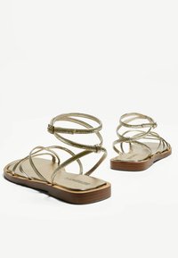 Sandales dorées à lanières avec une semelle plate, présentant des lanières croisées et une finition métallique lisse. Idéales pour une tenue décontractée d'été.