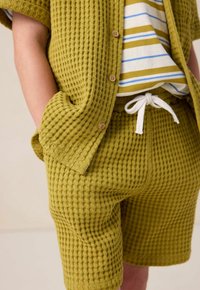 Tenue en coton texturé vert olive comprenant une chemise à manches courtes avec des boutons, un short assorti avec une taille élastique et un cordon de serrage.